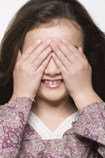 Smiling girl (8-9) covering her eyes, studio shot. Photo : Rob Lewine