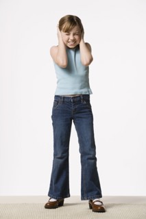Smiling girl (8-9) covering her ears, studio shot. Photo : Rob Lewine