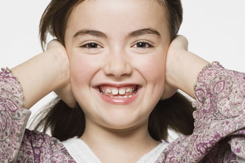 Smiling girl (8-9) covering her eyes, studio shot. Photo : Rob Lewine