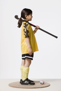 Studio portrait of girl (8-9) wearing sports clothes and holding hockey stick. Photo : Rob Lewine