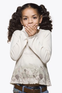 Studio portrait of girl (8-9) with pigtails covering mouth with hands. Photo : Rob Lewine