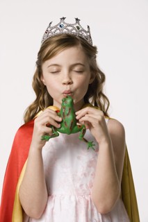 Studio portrait of girl (8-9) wearing princess costume and kissing toy frog. Photo: Rob Lewine