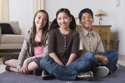 Portrait of happy children (8-9, 10-11) sitting on floor. Photo : Rob Lewine