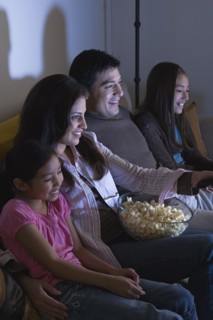 Family with two daughters (8-9, 10-11) watching tv on sofa. Photo : Rob Lewine