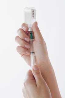 Close up of doctor's hand preparing syringe for injection. Photo : Rob Lewine