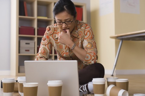 Woman working on laptop surrounded by empty coffee cups. Photo : Rob Lewine