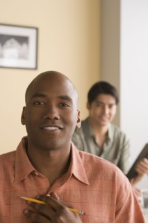Young businessman posing for portrait with colleague in background. Photo : Rob Lewine