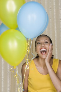 Happy mid adult african woman shouting while holding yellow and blue balloons. Photo : Rob Lewine