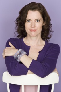 Portrait of smiling woman sitting on chair with purple background, studio shot. Photo : Rob Lewine