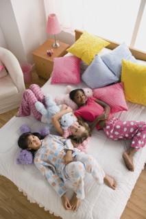 Three girls (10-11) lying on bed at slumber party. Photo : Rob Lewine