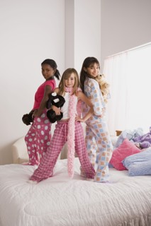 Portrait of three girls (10-11) standing on bed at slumber party. Photo: Rob Lewine