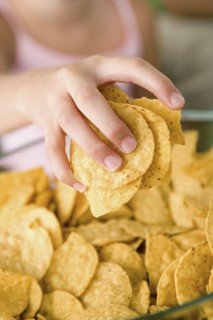 Close up of girl's (10-11) hand taking potato chips from bowl. Photo : Rob Lewine