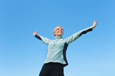 Woman with arms raised against blue sky. Photo : Tetra Images