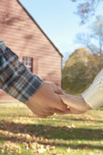 Close-up of couple holding hands in front of cottage house. Photo : Tetra Images