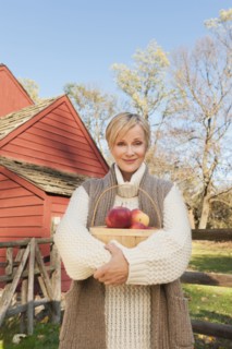 USA, New Jersey, Portrait of smiling woman holding basket with apples in front of cottage house in