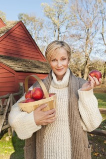 USA, New Jersey, Portrait of smiling woman holding basket with apples in front of cottage house in