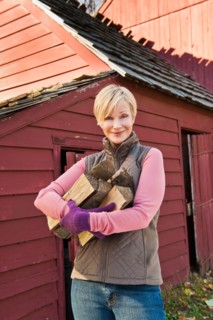 USA, New Jersey, Portrait of smiling woman holding firewood in front of cottage house in Autumn.