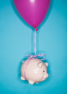 Studio shot of piggy bank lifted by balloon.