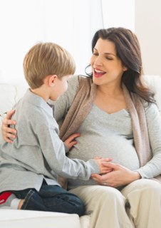 Boy (4-5) touching pregnant mother's belly.