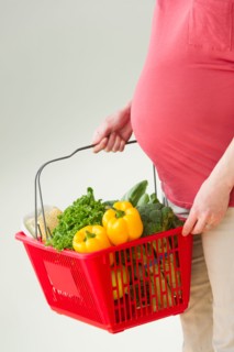 Studio shot of woman with shopping basket full of groceries, midsection.