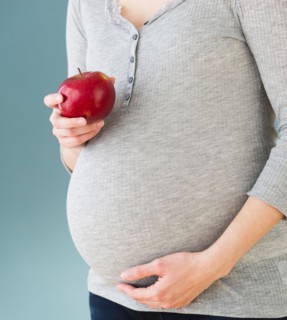 Studio shot of pregnant woman eating apple, midsection.