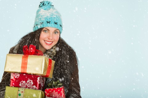 Studio portrait of woman in winter clothing carrying presents.