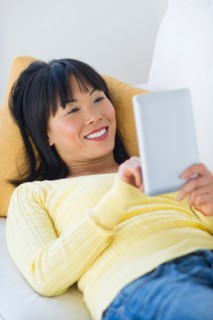 Smiling woman lying on sofa and using digital tablet.
