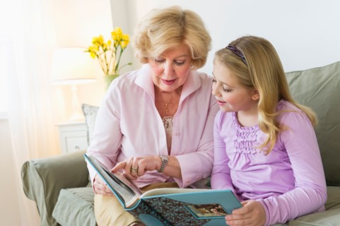 Grandmother with granddaughter (8-9) reading on sofa.