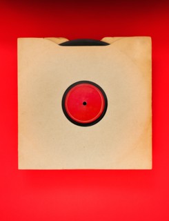Vinyl record in envelope on red background, studio shot.