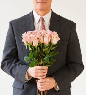 Close up of man in suit holding bouquet of roses, studio shot.