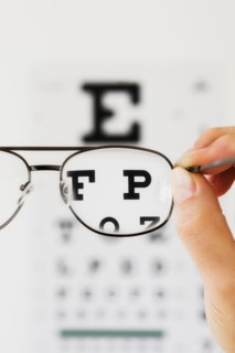 Close up of hand holding glasses above eye chart, studio shot.