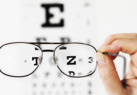 Close up of hand holding glasses above eye chart, studio shot.
