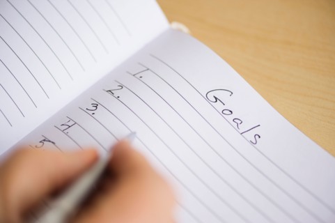Close up of man's hand writing New Years resolution in notebook, studio shot.