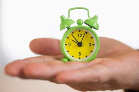 Close up of man's hand holding alarm clock, studio shot.