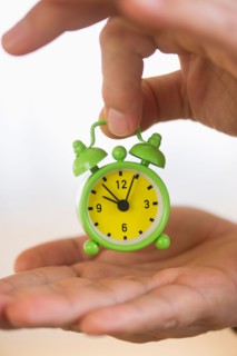 Close up of man's hand holding alarm clock, studio shot.