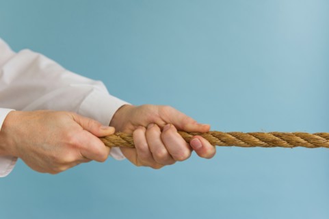 Close up of man's hands pulling rope, studio shot.