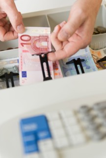 Close up of man's hand putting banknotes into cash register, studio shot.