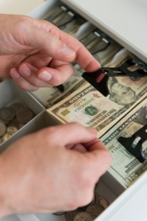 Close up of man's hand putting banknotes into cash register, studio shot.