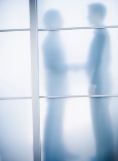 Silhouettes of two businessmen behind glass door.