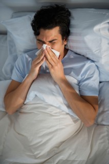 Man lying in bed and blowing nose.