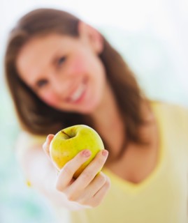 Smiling young woman holding apple. Photo : Daniel Grill