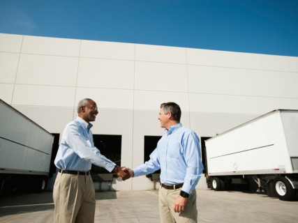 Business men shaking hands outside warehouse.