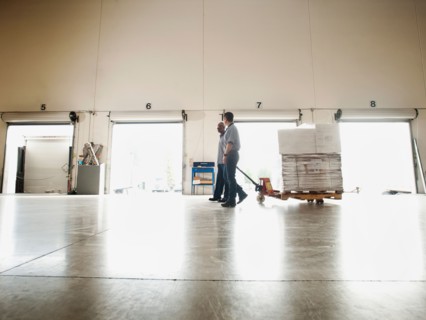 Two men pulling hand truck across warehouse.