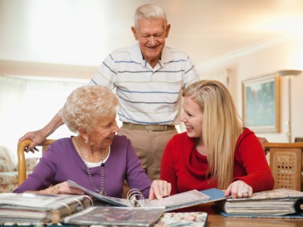 Senior couple and mid adult woman watching family scrapbooks.