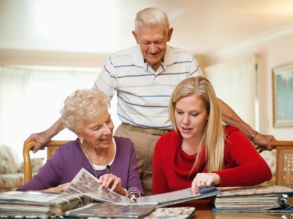 Senior couple and mid adult woman watching family scrapbooks.