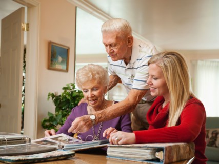 Senior couple and mid adult woman watching family scrapbooks.