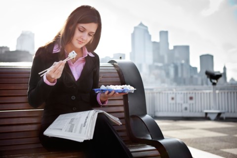 USA, Seattle, Young businesswoman eating sushi and reading newspaper. Photo : Take A Pix Media