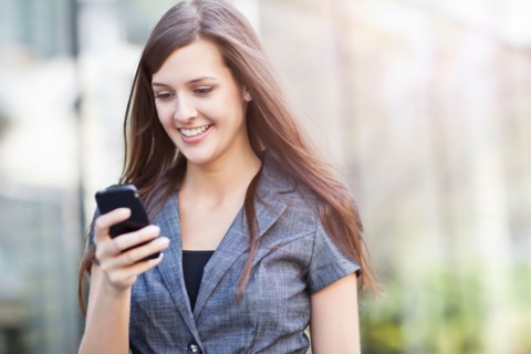 Young elegant woman standing and using mobile phone. Photo : Take A Pix Media