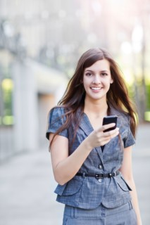Young elegant woman standing and using mobile phone. Photo : Take A Pix Media