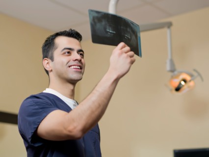 Smiling dentist in surgery checking x-ray . Photo : Dan Bannister